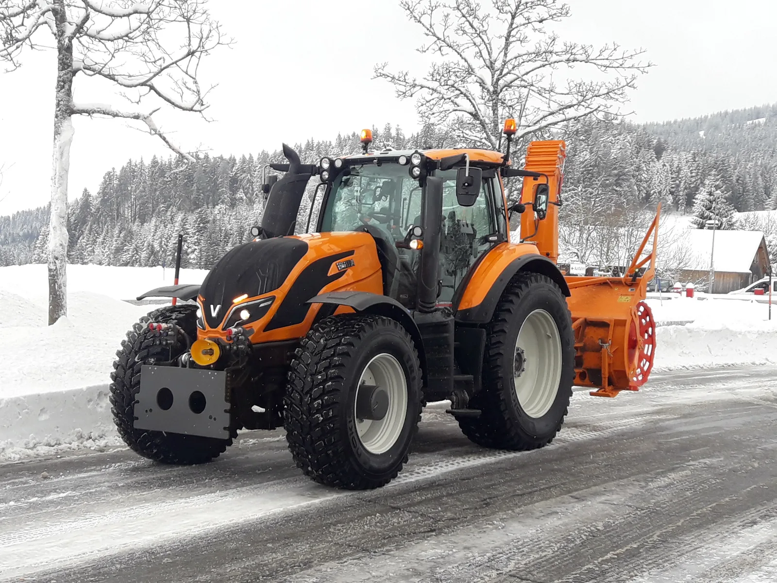 Oranger Valtra mit Schneefräse im Winterdienst auf einer verschneiten Straße